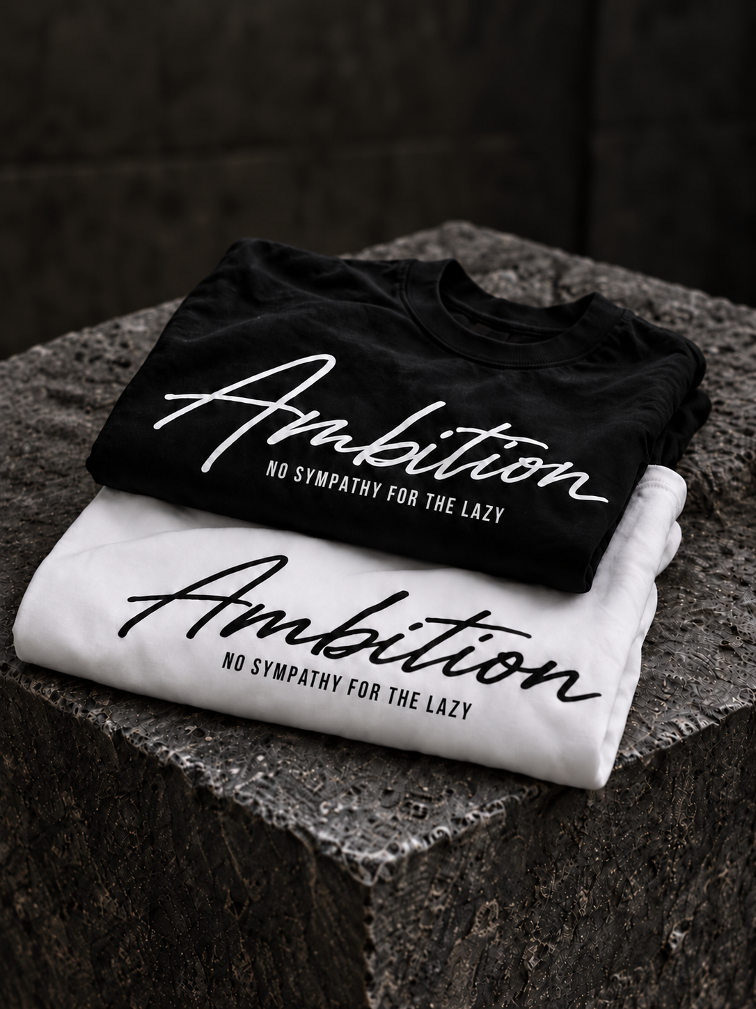 Black and white Ambition T-shirts folded on stone.