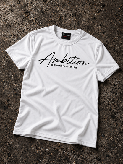 White Ambition T-shirt laid flat on dark textured concrete, showing the black chest print, small tagline and sewn neck label.